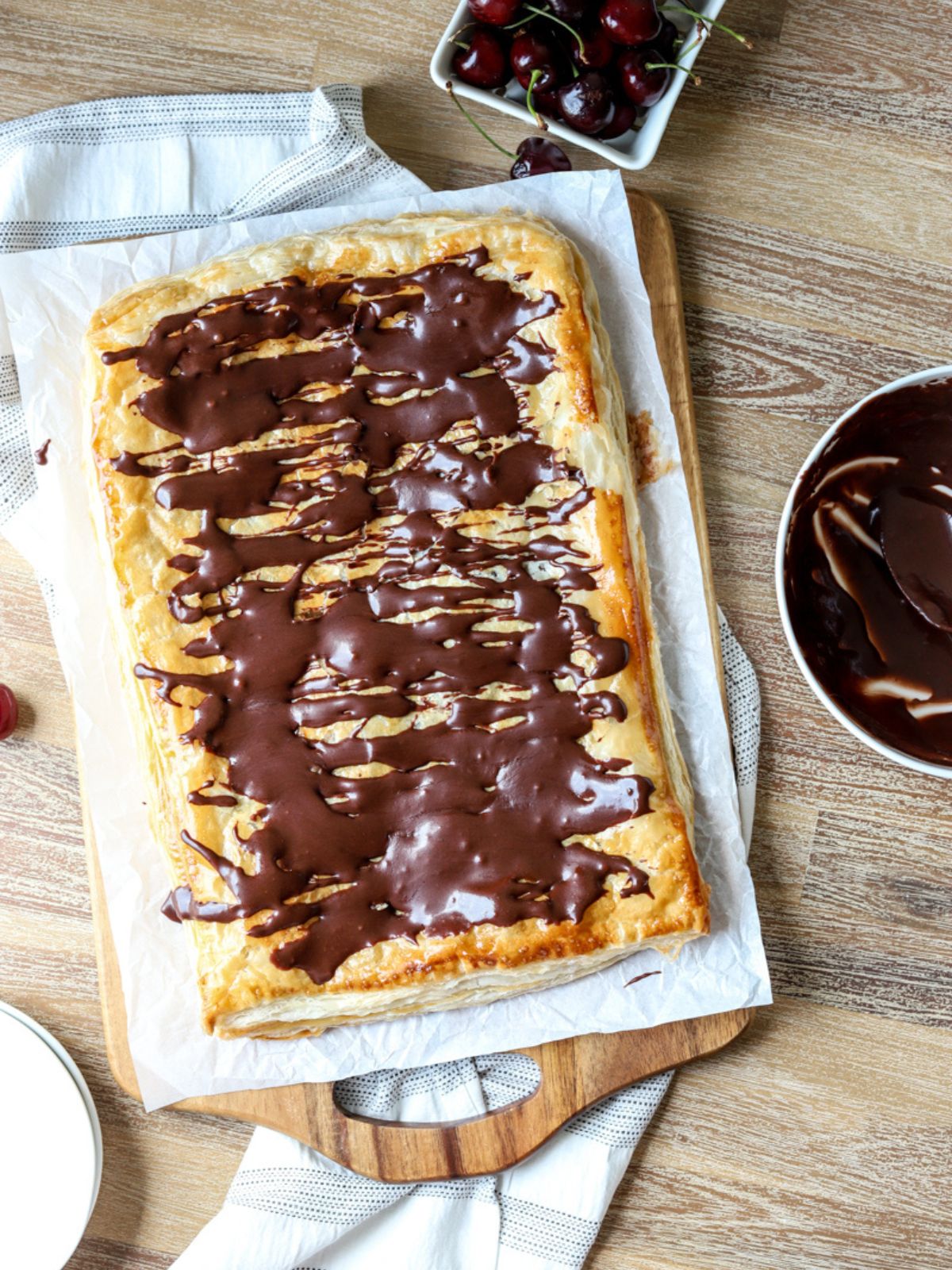 A giant slab pie on parchment paper and a bowl of cherries.