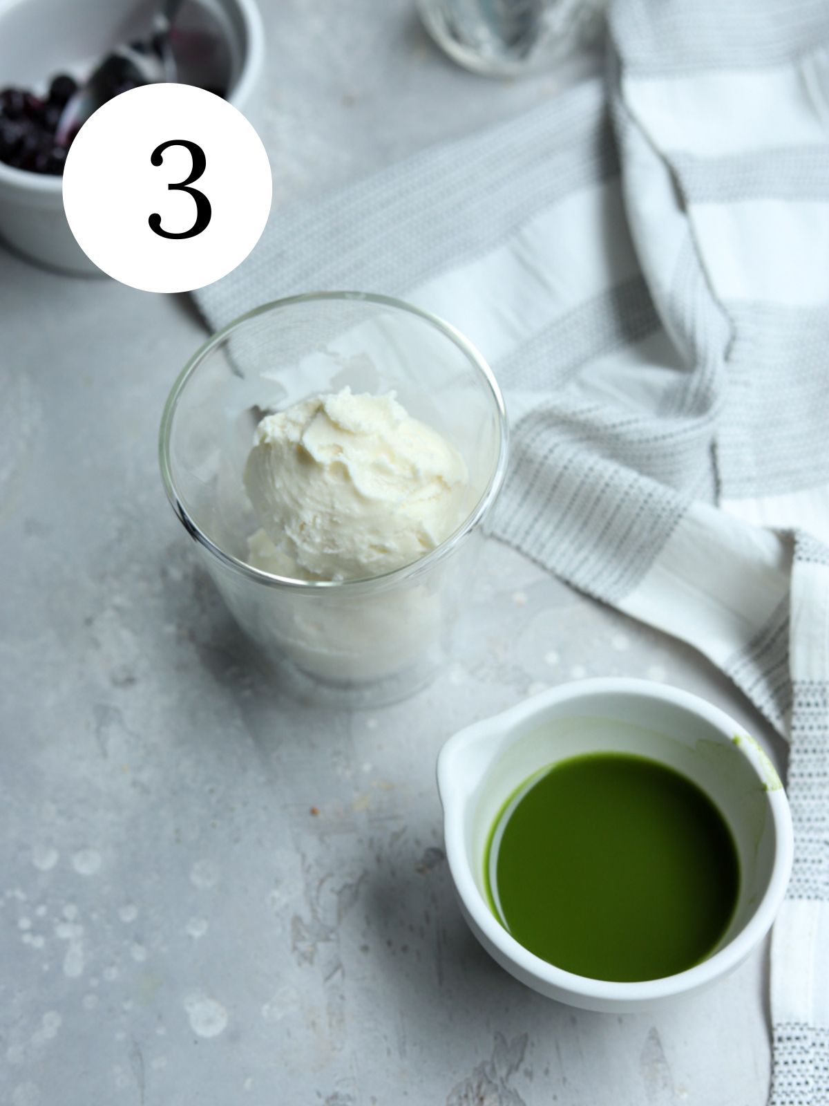 A glass of ice cream, a cup with matcha tea and a kitchen towel.