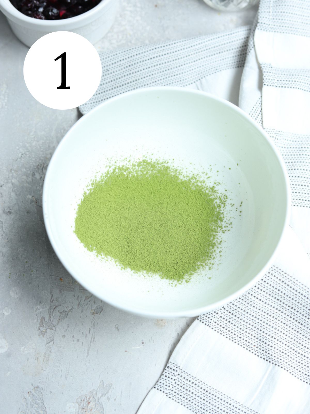 Matcha powder in a white bowl next to a kitchen towel.