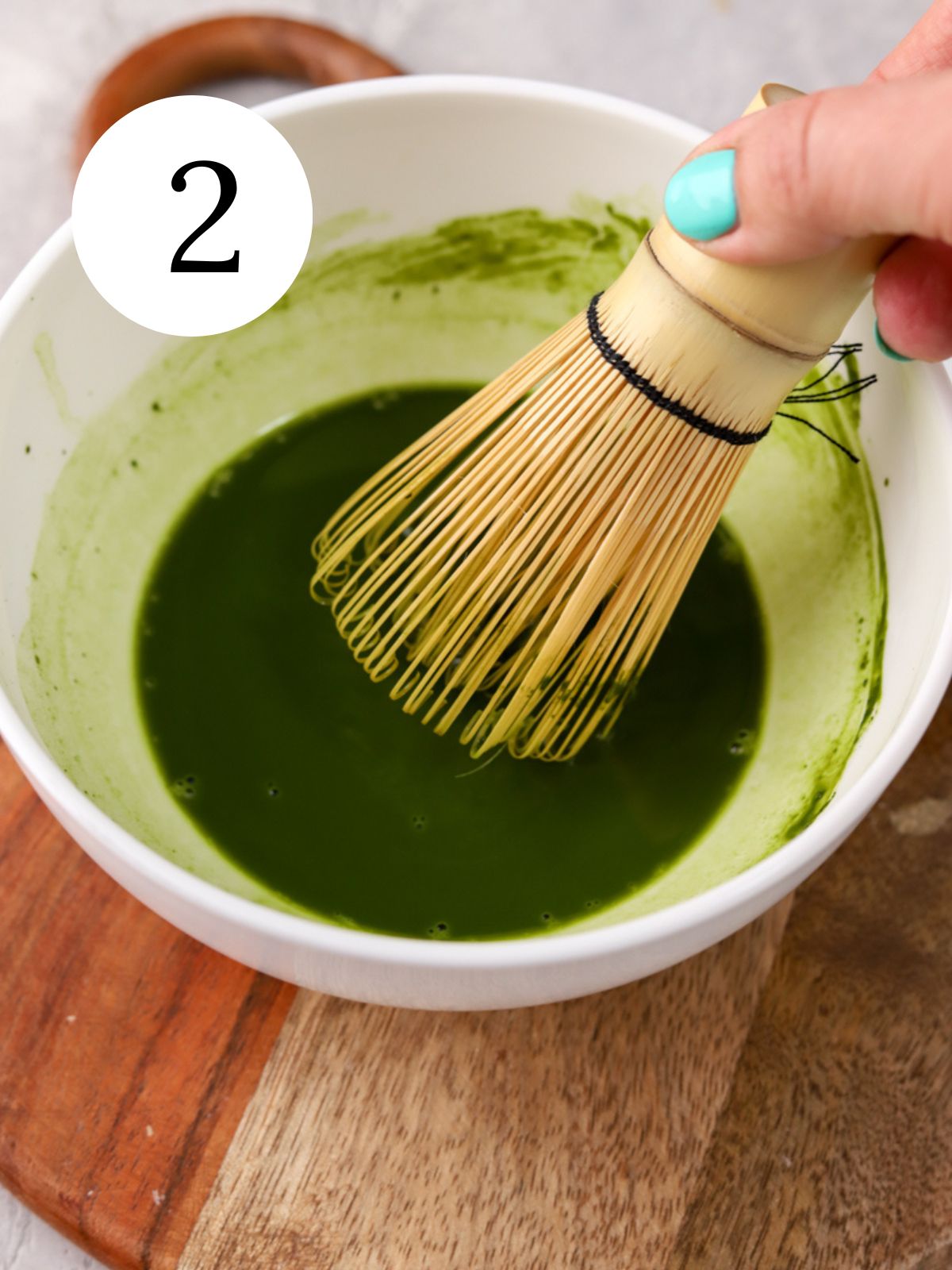 A white bowl with matcha being stirred together with a traditional matcha whisk.