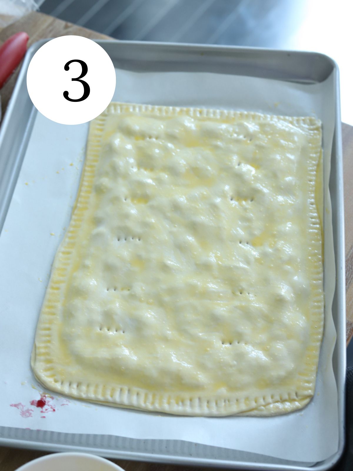 A giant pop tart brushed with egg wash on a baking sheet.