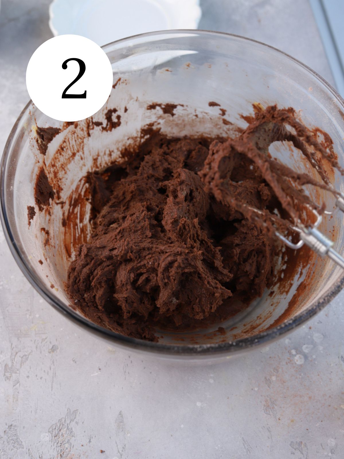 Chocolate cookie dough in a glass bowl with an electric mixer.