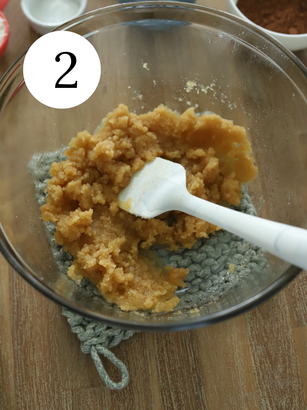 A glass bowl with butter and sugar combined with a spatula.