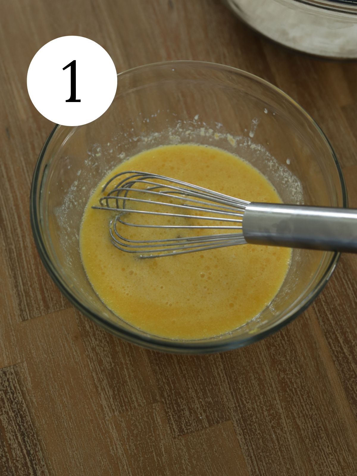 A glass mixing bowl with batter and a whisk. 