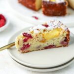 A slice of cake with raspberries and peaches on a small plate.