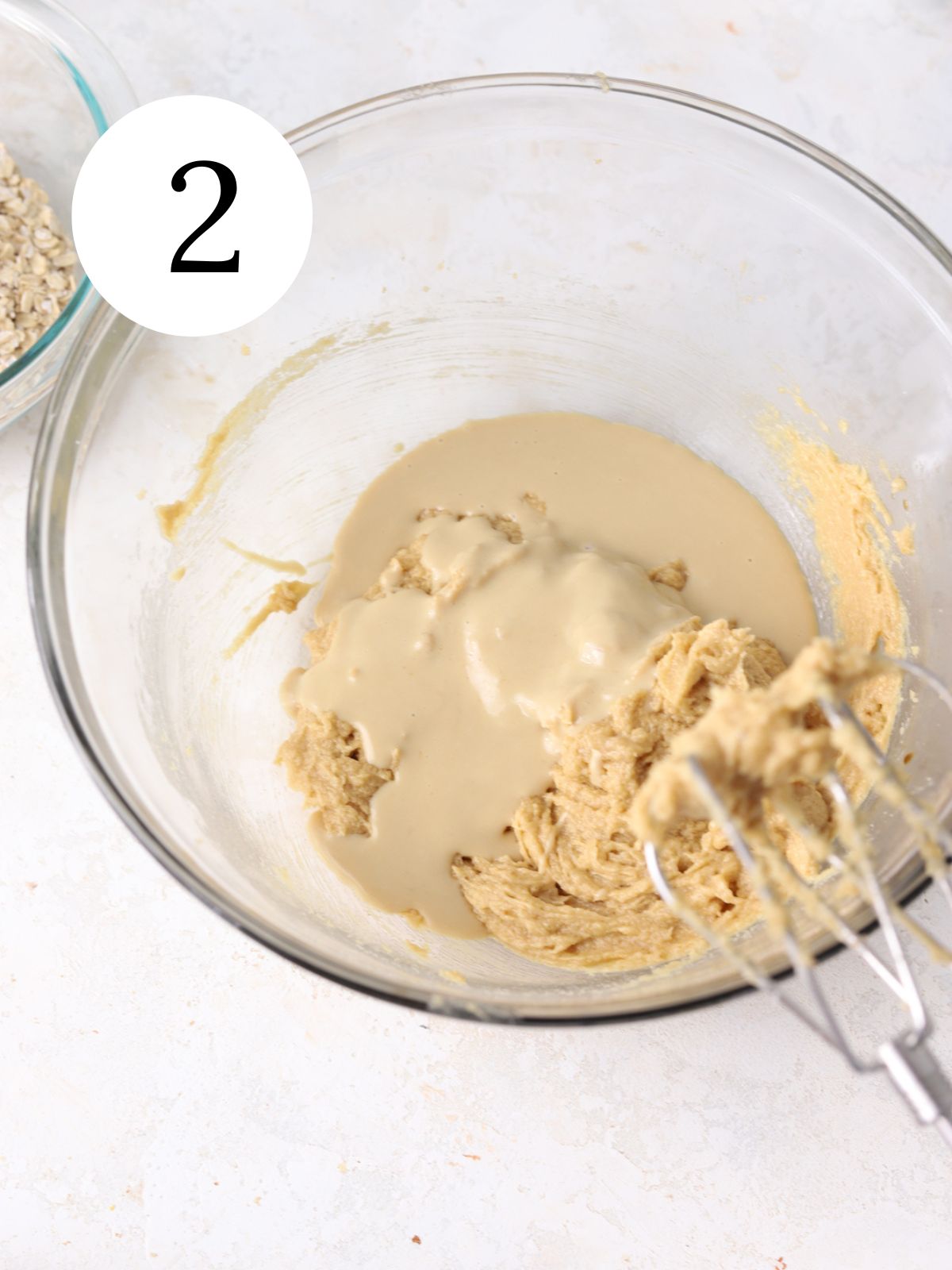 A large glass mixing bowl with tahini poured over cookie dough.
