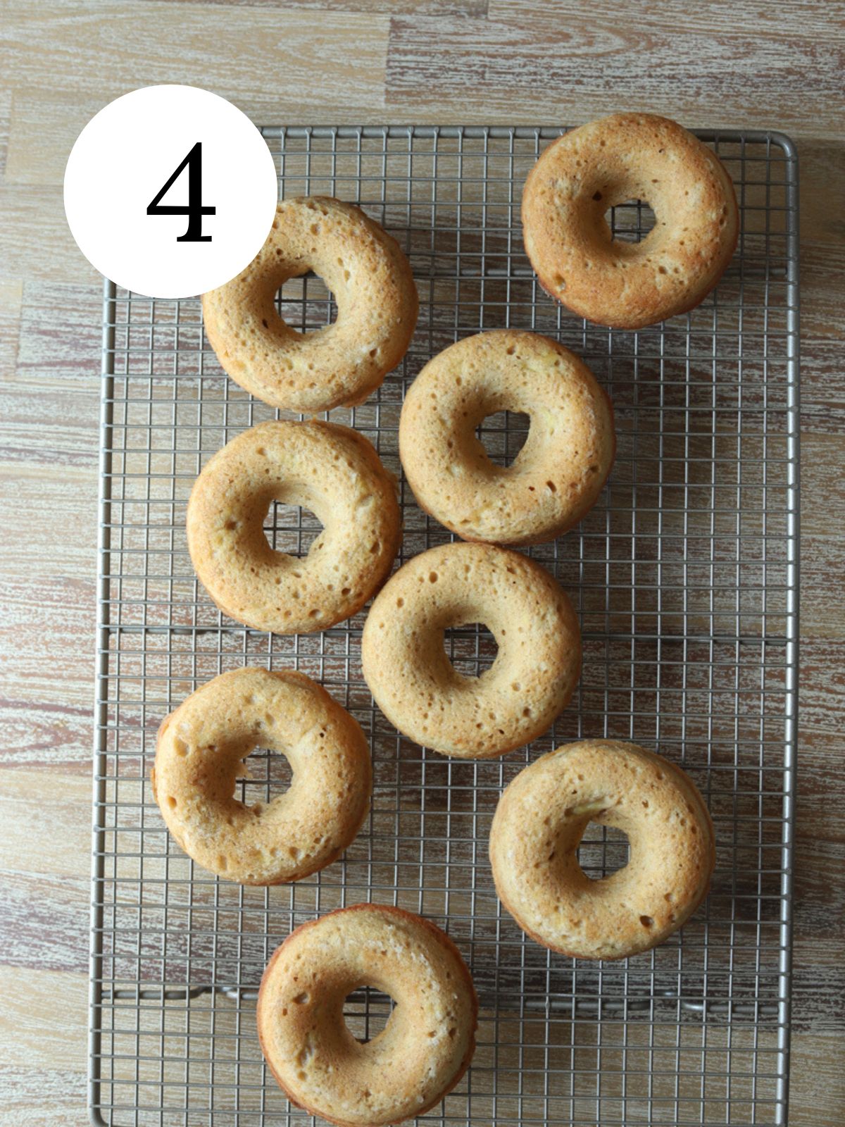 Baked donuts on a wire cooling rack on a wooden table.