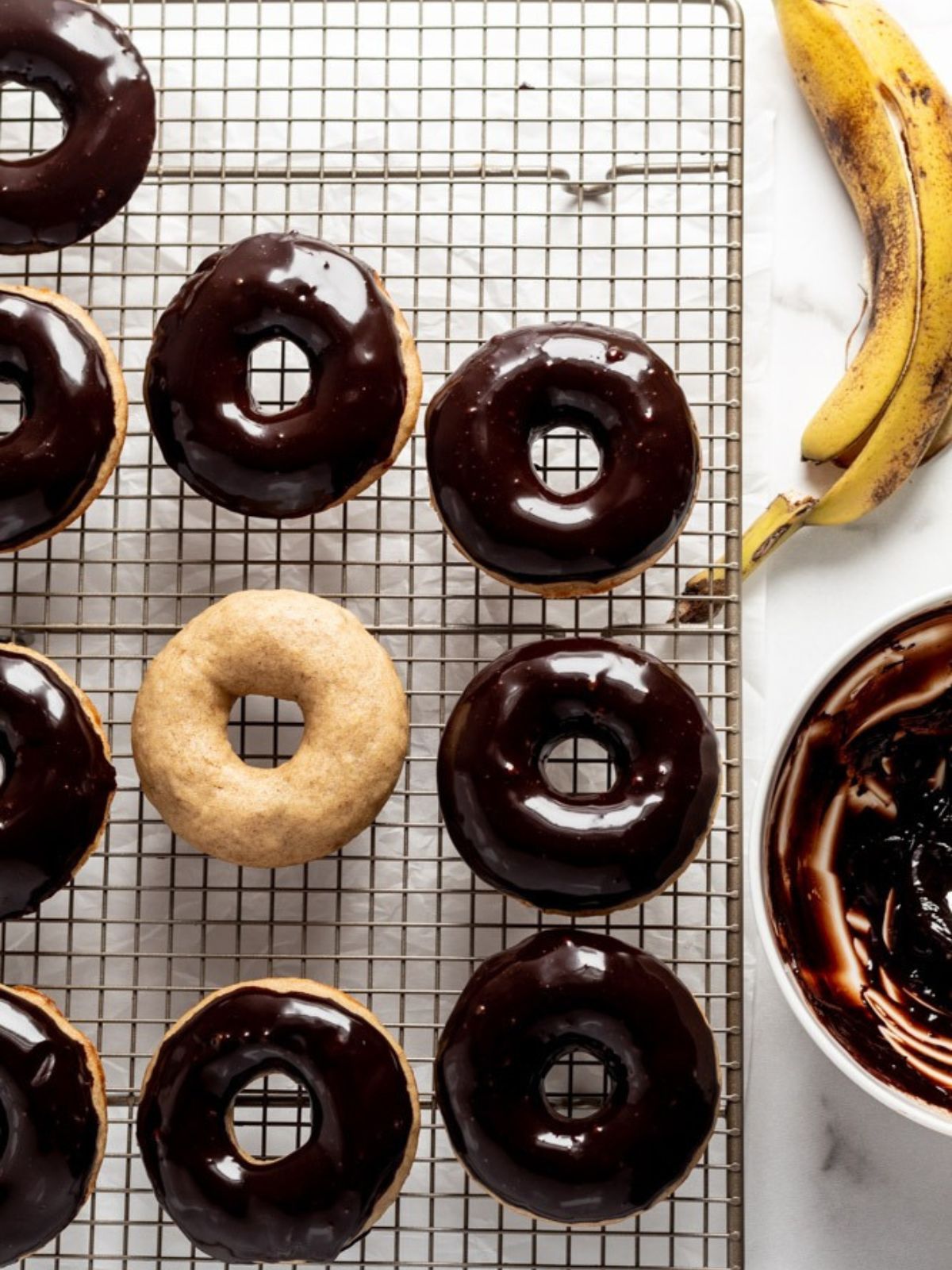 Donuts topped with chocolate ganache on a rack next to a banana.