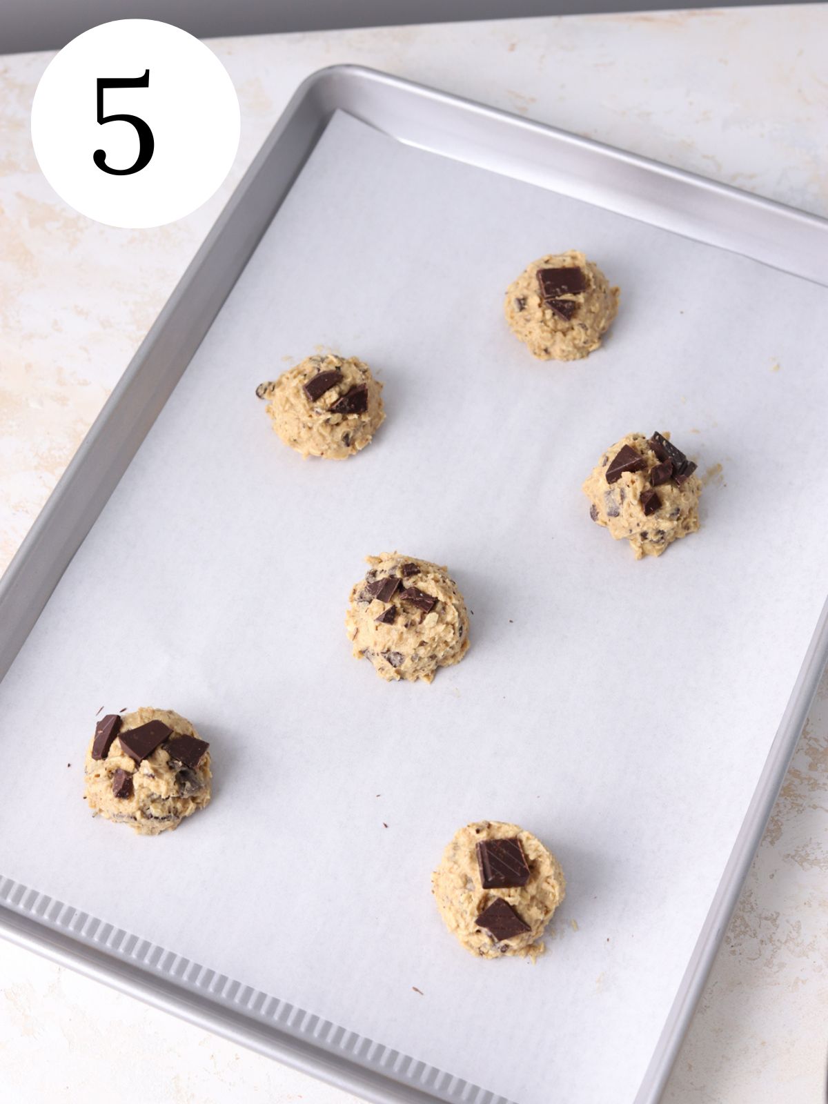 A baking sheet lined with parchment paper with cookie dough balls on it.