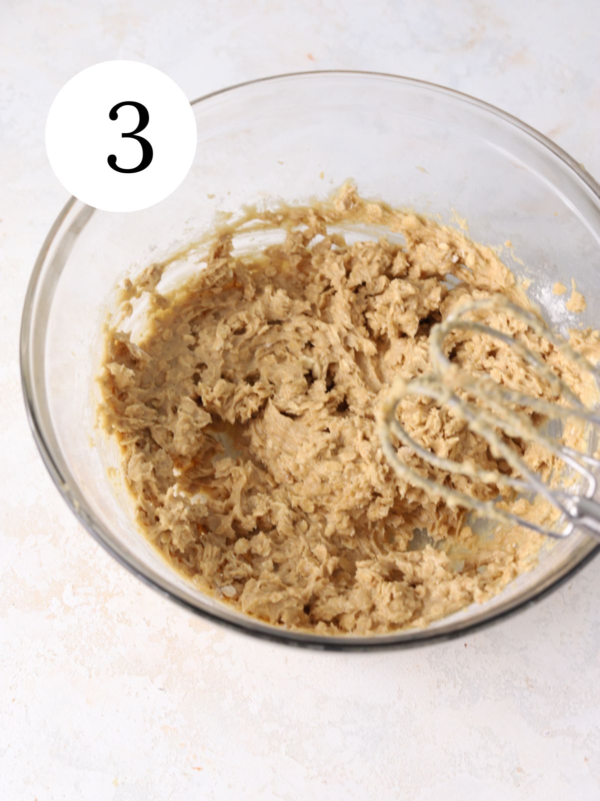 A glass bowl with cookie dough and an electric mixer.