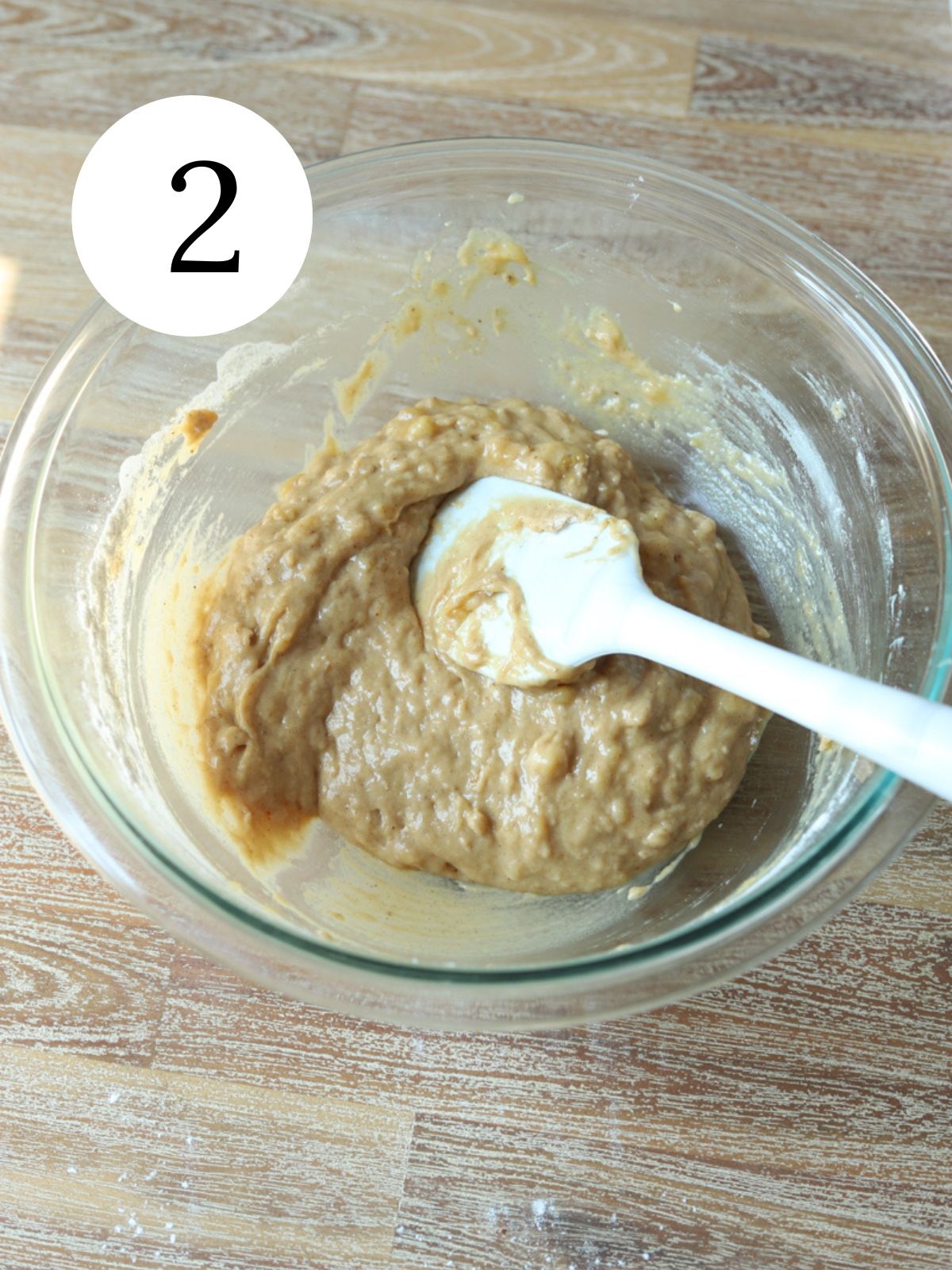 A glass bowl with brown batter and a spatula in it.