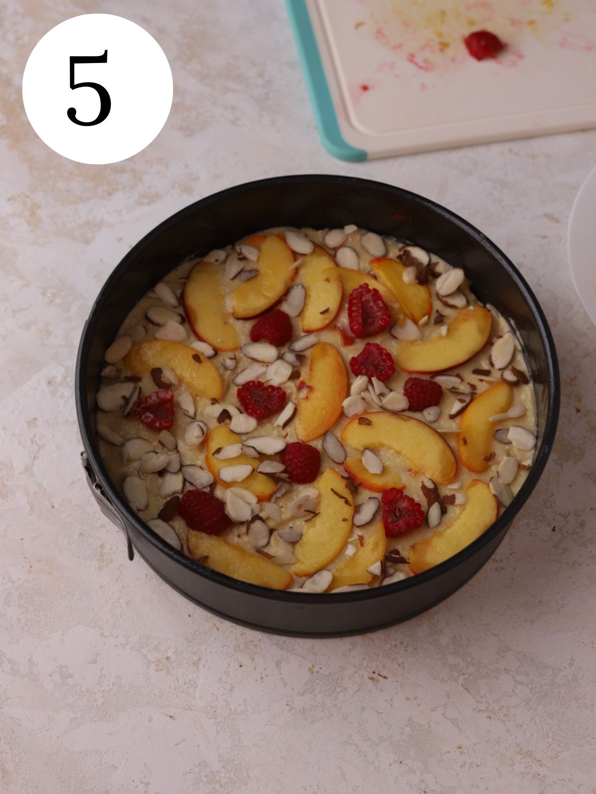 A springform pan with raspberries and peaches on cake batter.