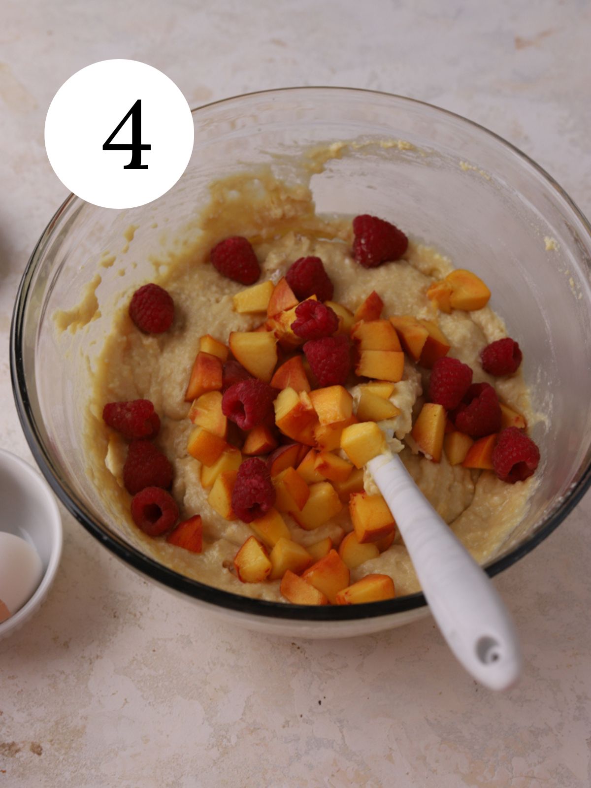 A mixing bowl with fruit being stirred into cake batter with a spatula.