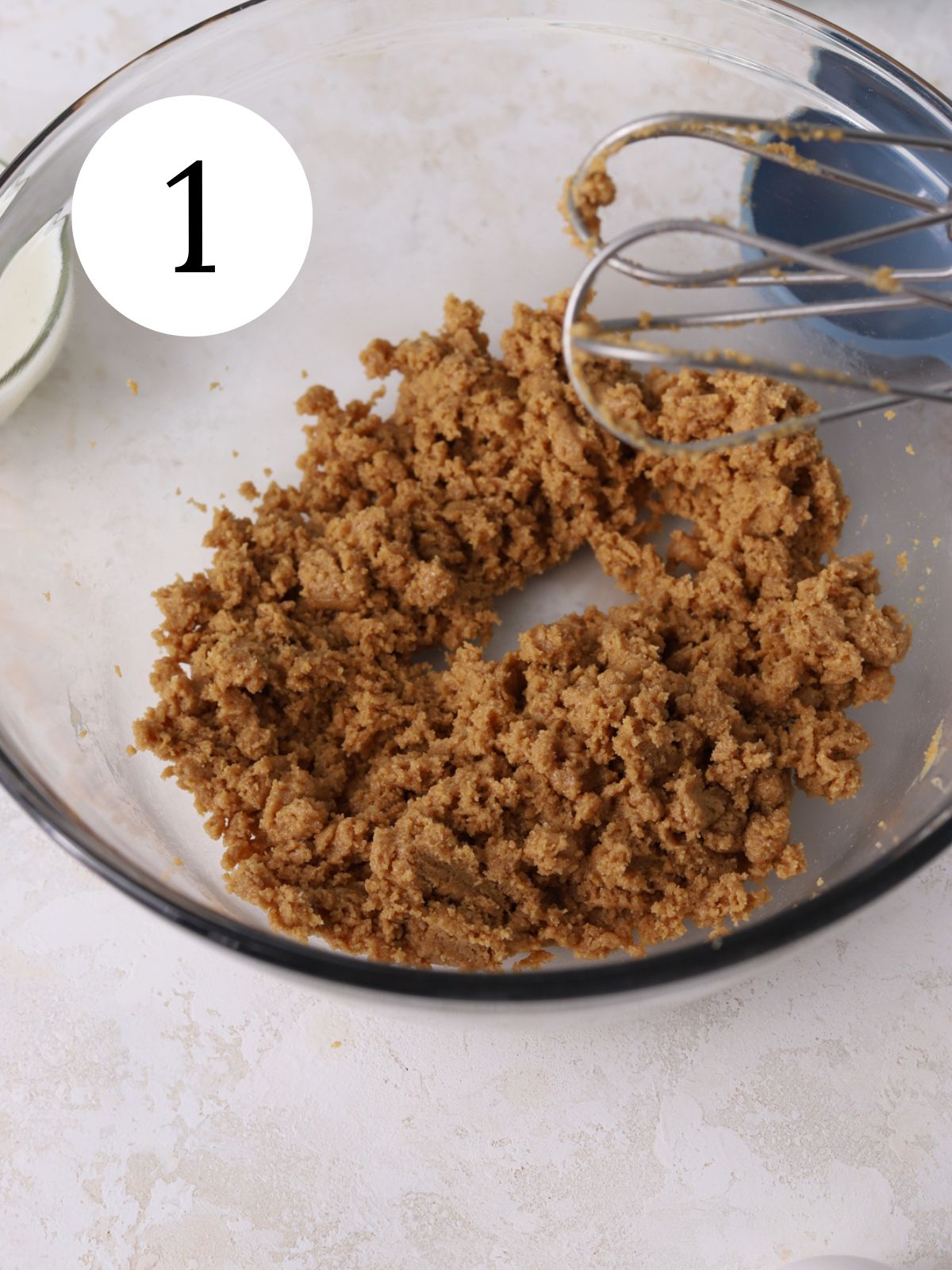 Sugars and peanut butter beat together in a glass bowl with an electric mixer.