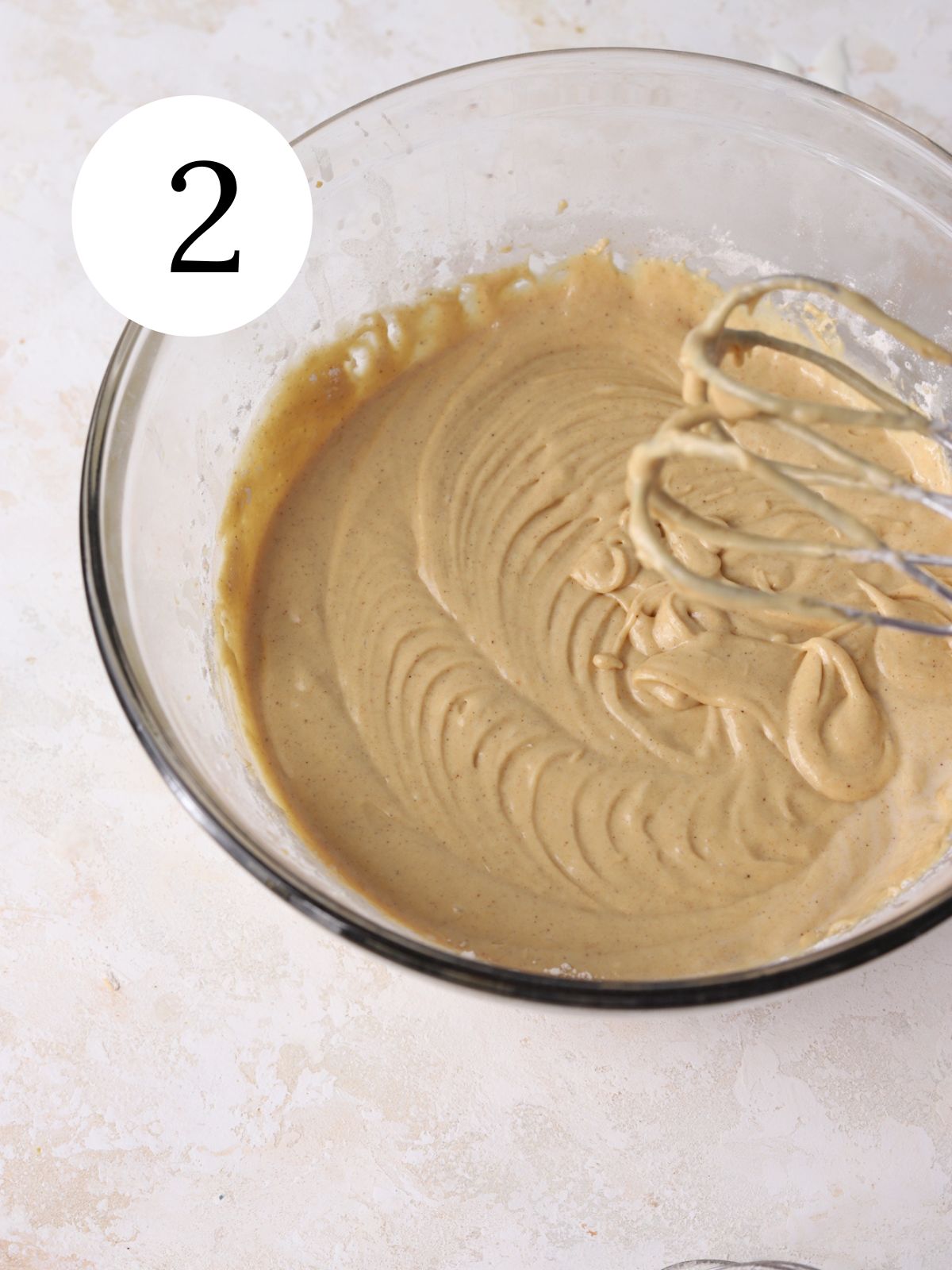 A glass bowl with batter being mixed together with an electric mixer.