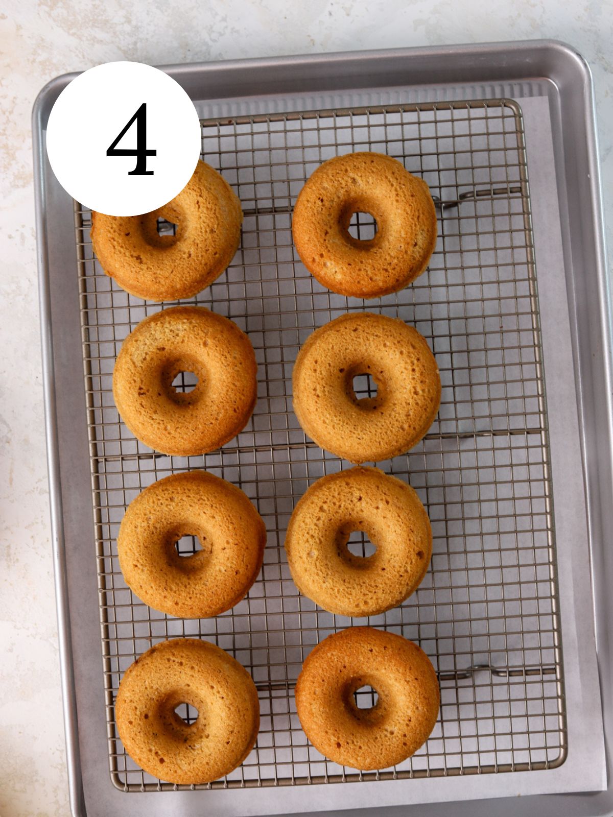 Eight baked donuts on a wire rack set on a baking sheet. 