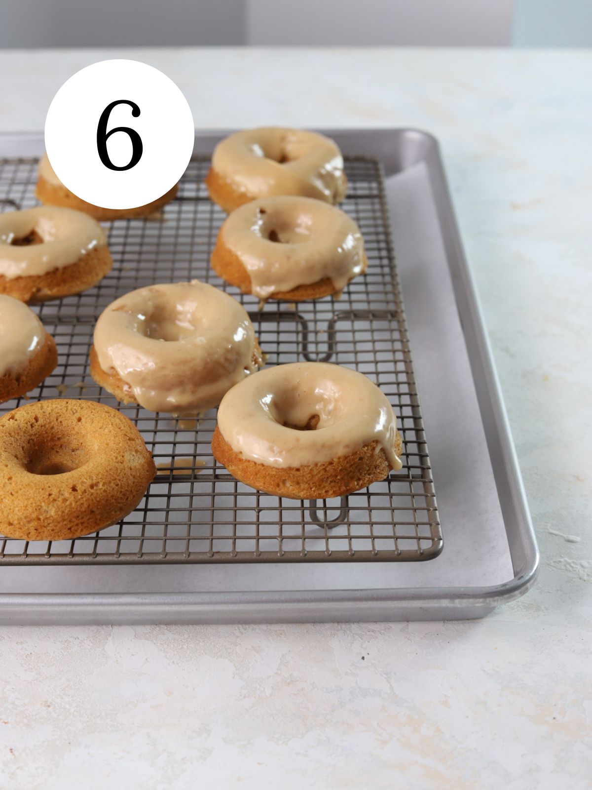 Donuts with peanut butter glaze on top on a wire rack set on a baking sheet.