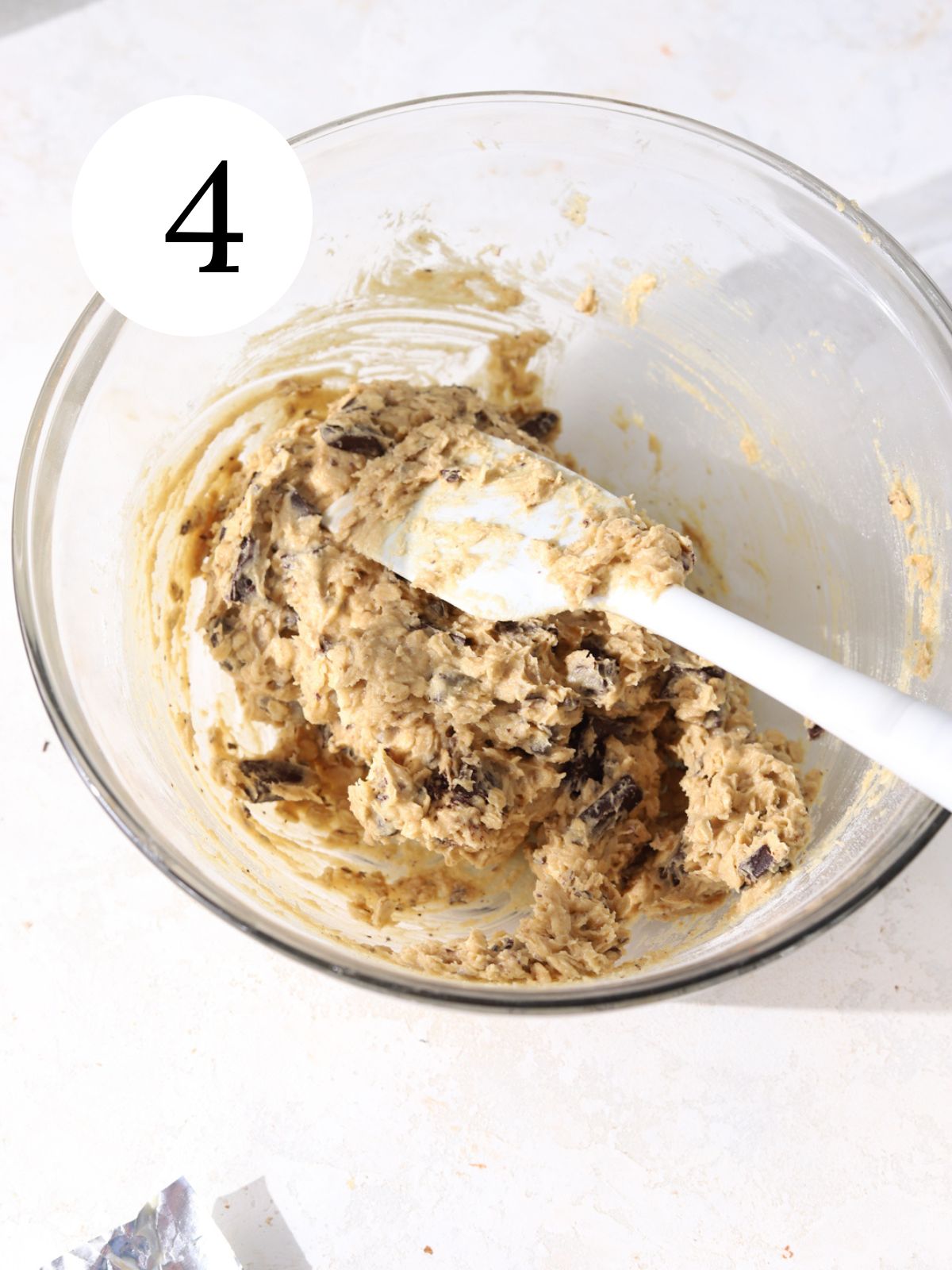 Chocolate chip cookie dough being stirred with a spatula in a large bowl.