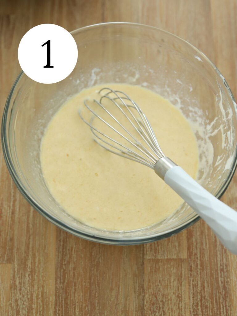 Wet ingredients and a whisk in a glass bowl. 