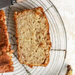 Piece of banana bread on a wire rack next to a knife.