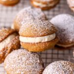 Pumpkin whoopie pies dusted with powdered sugar on a wire rack.