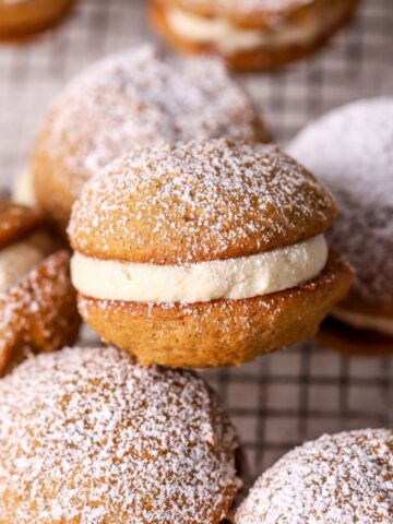 Pumpkin whoopie pies dusted with powdered sugar on a wire rack.