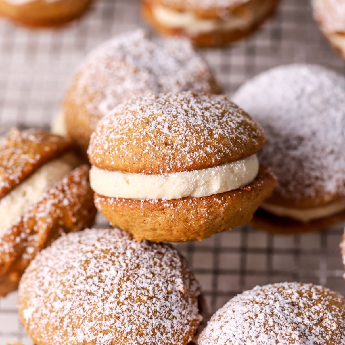 Pumpkin whoopie pies dusted with powdered sugar on a wire rack.