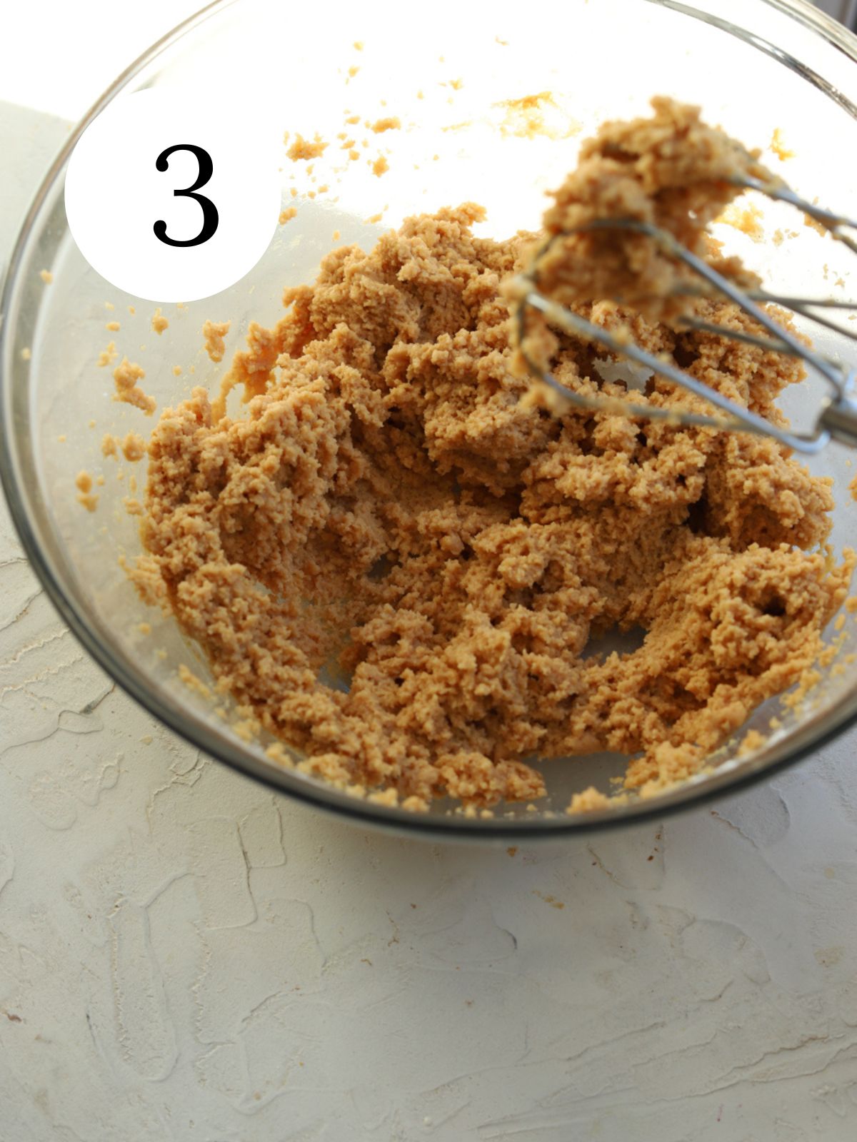 A glass mixing bowl with peanut butter and a mixer. 