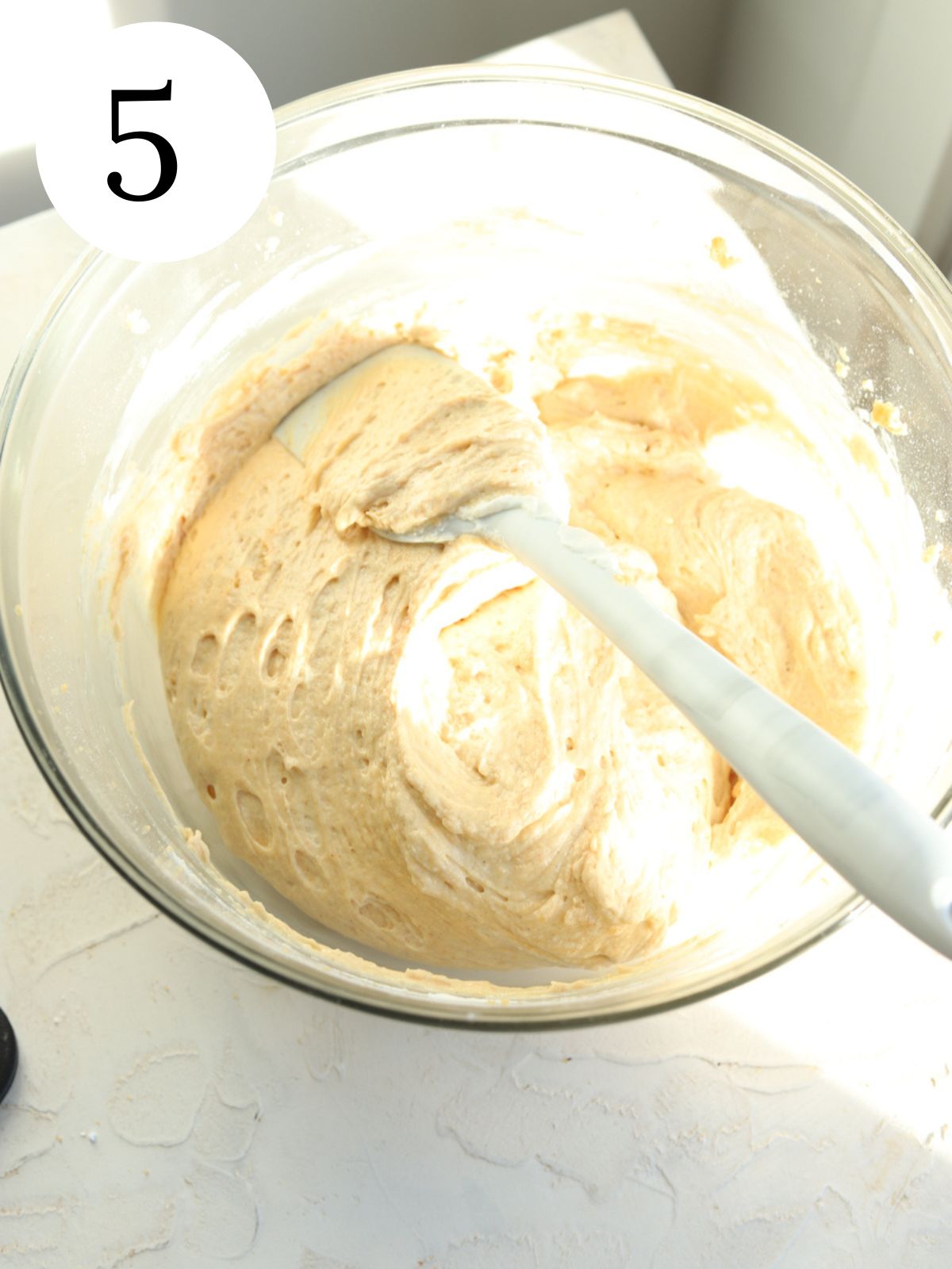 A glass mixing bowl with peanut butter and a spatula.
