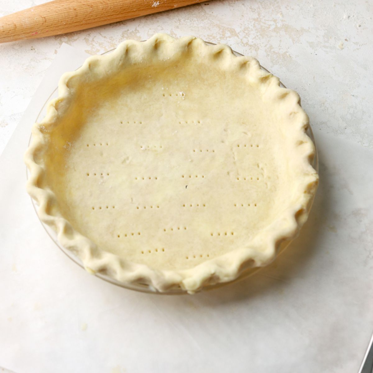 Crimped pie dough in a pie dish next to a rolling pin.