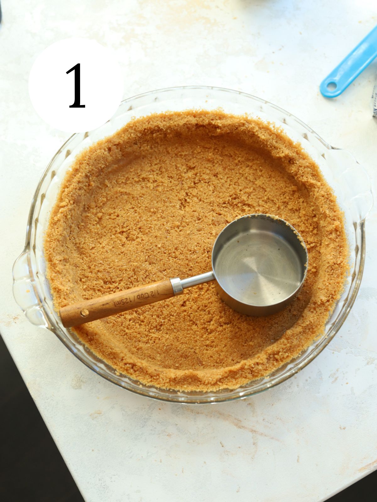 A pie plate with a cookie crust and a measuring cup.