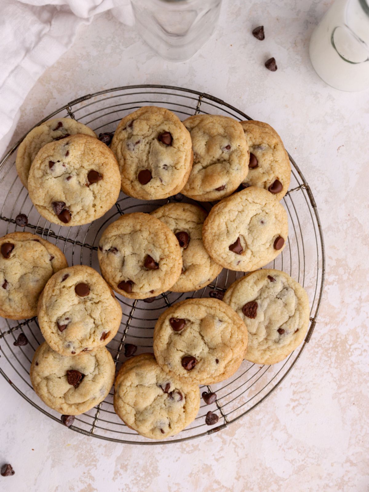 A batch of chocolate chip cookies on a baking rack and some milk jugs.