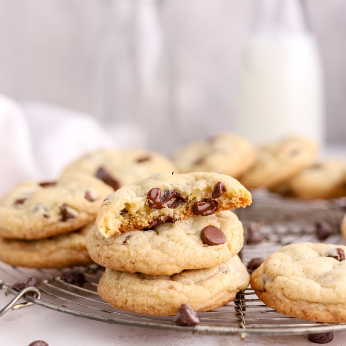 Chocolate chip cookies on a round rack next to some milk.