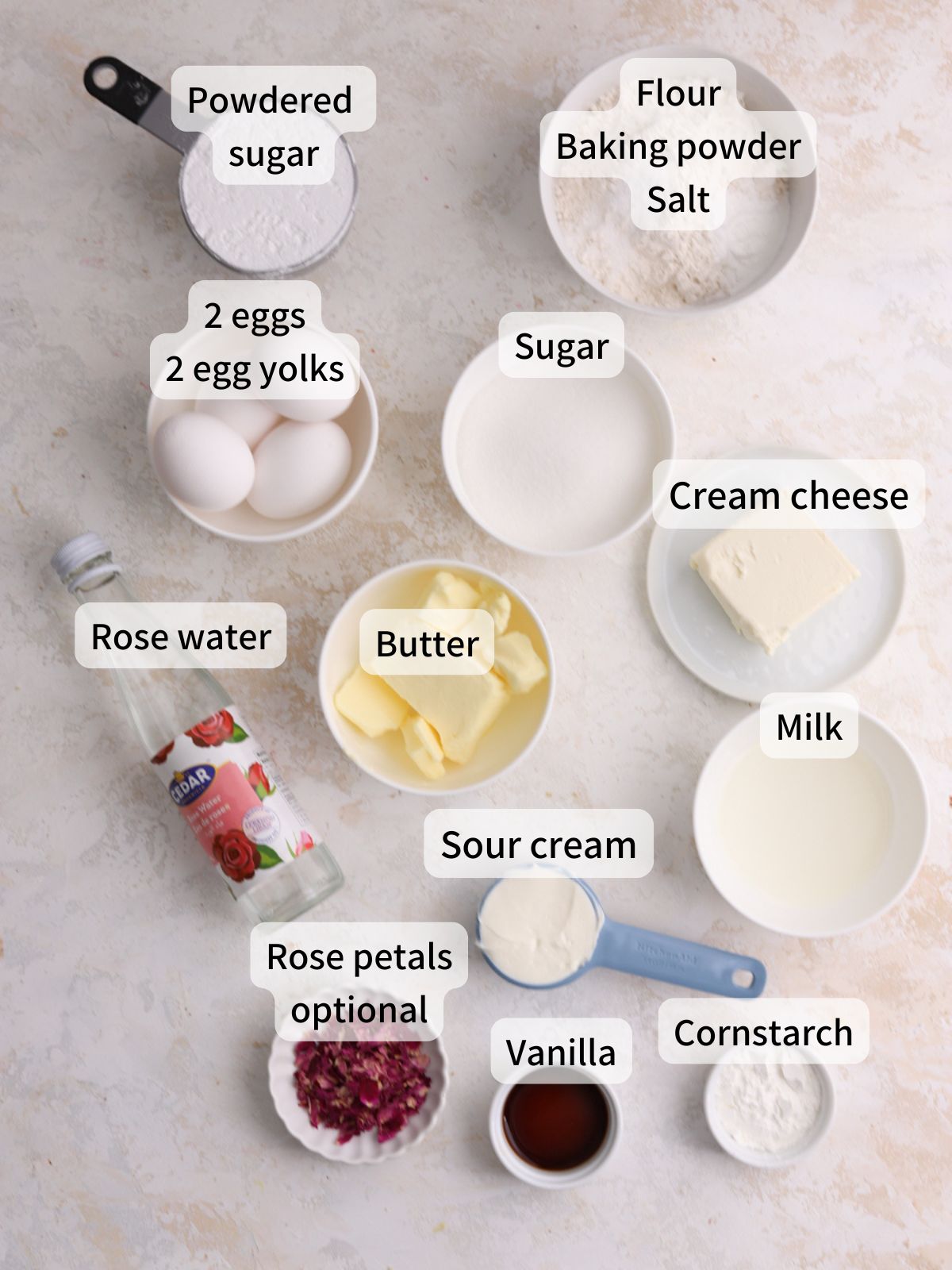 Labeled ingredients needed to make rose cupcakes laid out on a table.