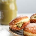 A golden brown donut filled with pistachio spread on a plate.