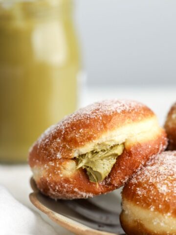 A golden brown donut filled with pistachio spread on a plate.
