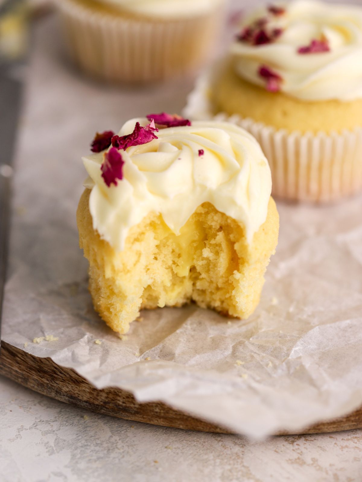 A cupcake topped with frosting and rose petals with a bite taken out of it.