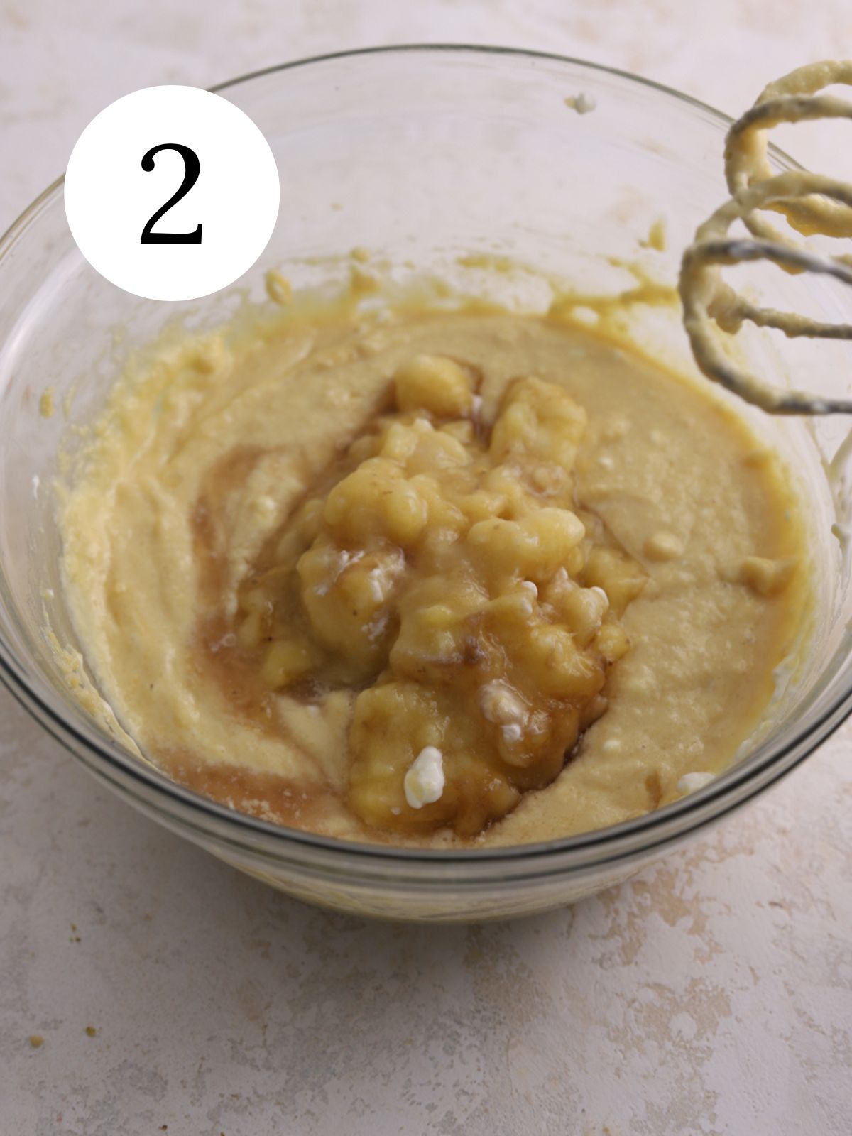 A mixing bowl with mashed banana being adding to batter.
