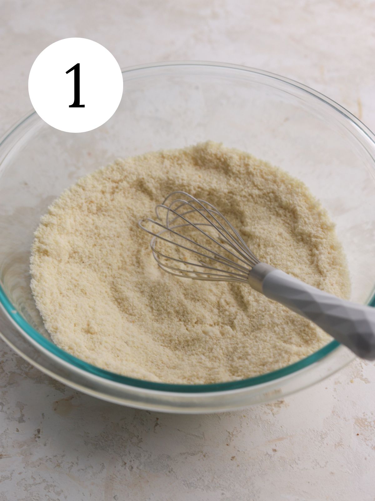 A glass mixing bowl with almond flour and a whisk. 