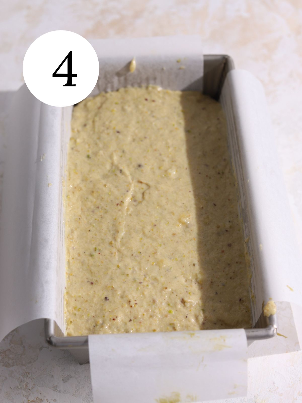 A loaf pan with pistachio banana bread spread in it.
