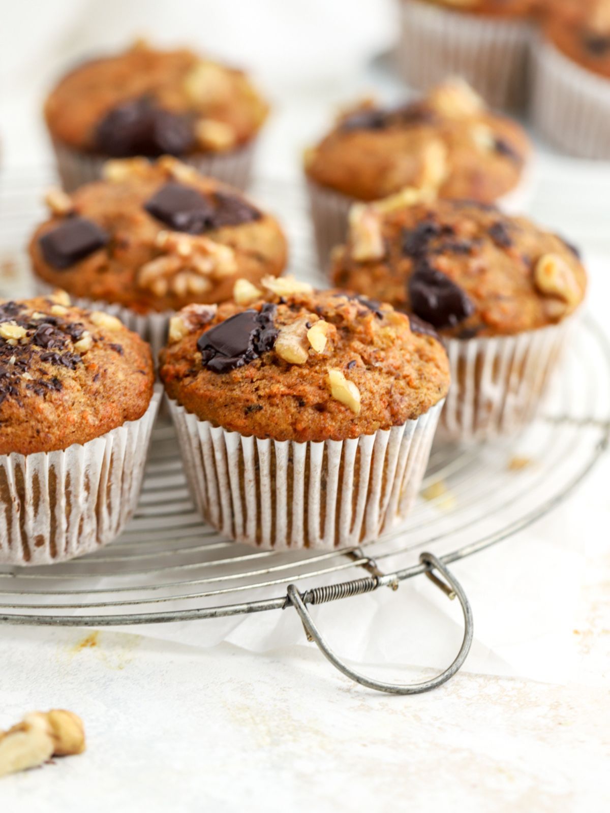 Carrot muffins topped with walnuts and chocolate on a round wire rack.