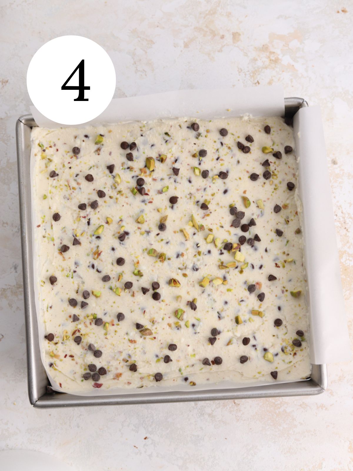 A square pan filled with a ricotta mixture topped with chocolate chips and pistachios.