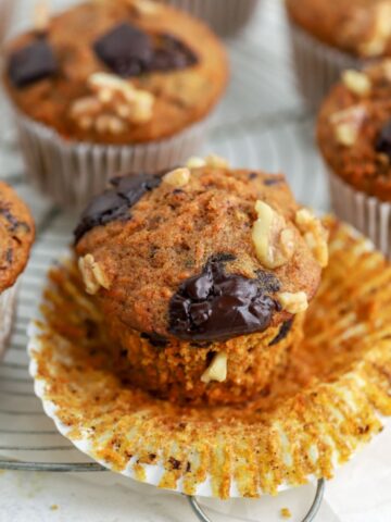 Carrot muffins topped with walnuts and chocolate on a rack.