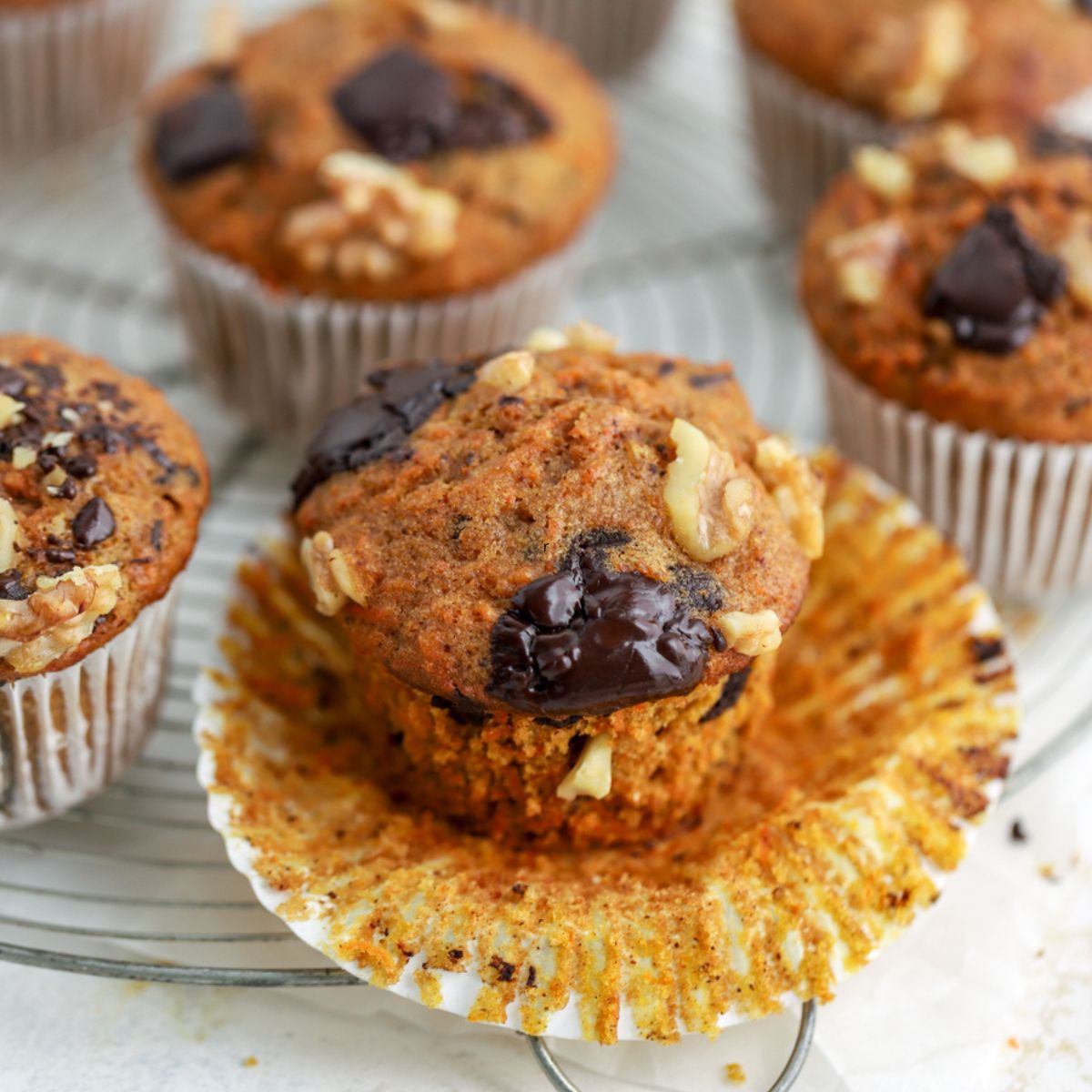 Carrot muffins topped with walnuts and chocolate on a rack.