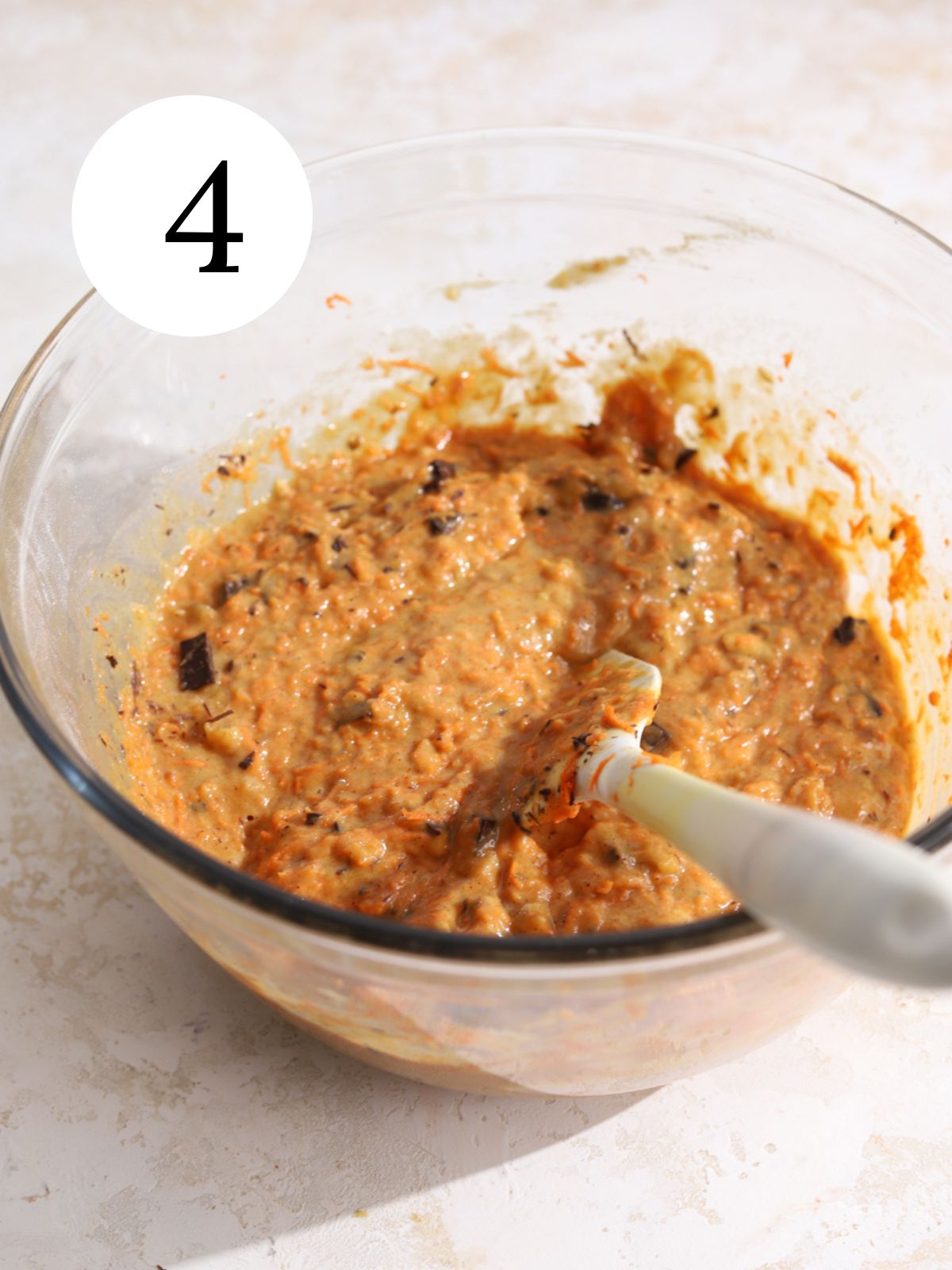 Carrot muffin batter in a glass bowl with a spatula.
