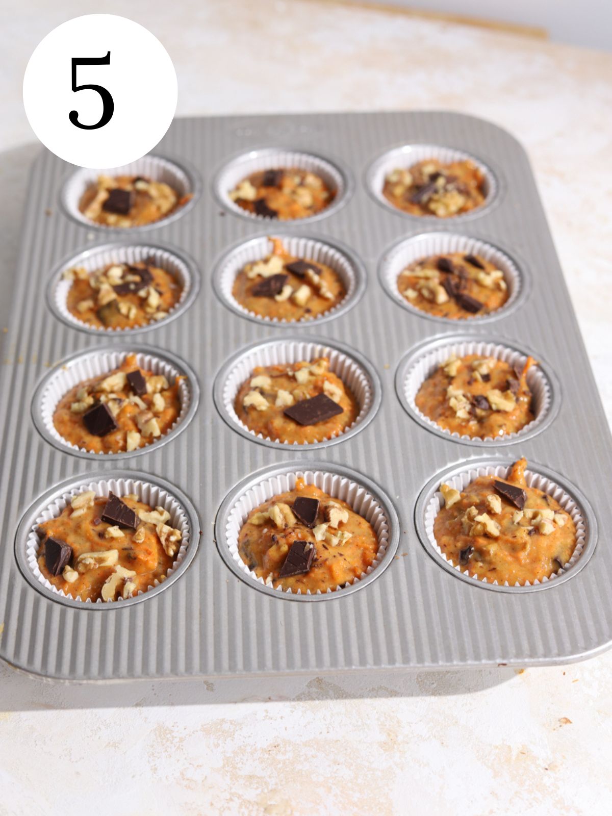 A muffin pan lined with paper liners filled with carrot muffin batter.