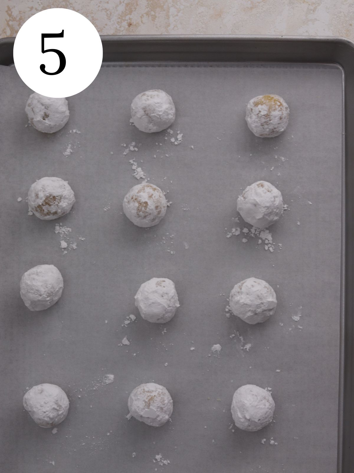 Cookie dough balls coated with powdered sugar on a baking sheet. 