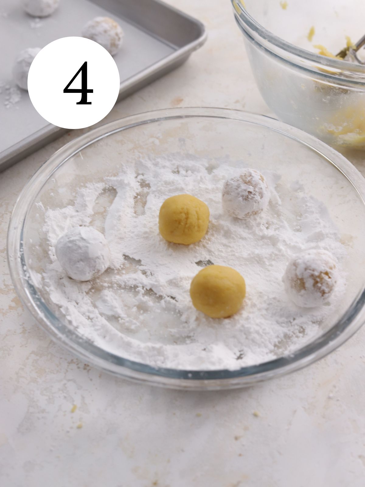 Cookie dough balls rolled in powdered sugar in a glass pie plate. 