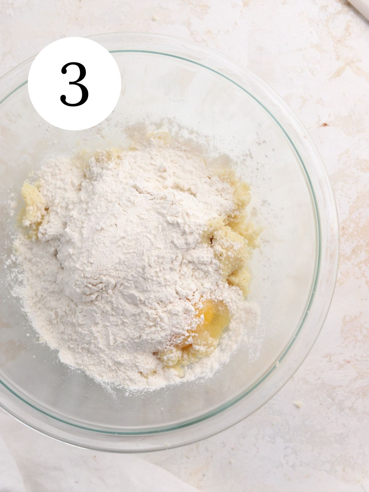 A glass bowl with flour and eggs on top of cookie dough. 