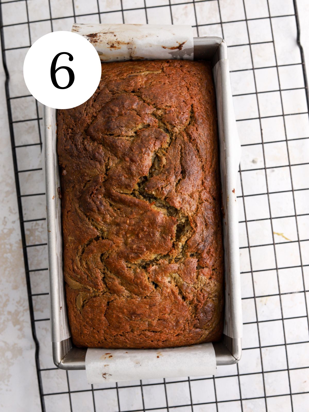Banana bread in a pan set on a wire rack.
